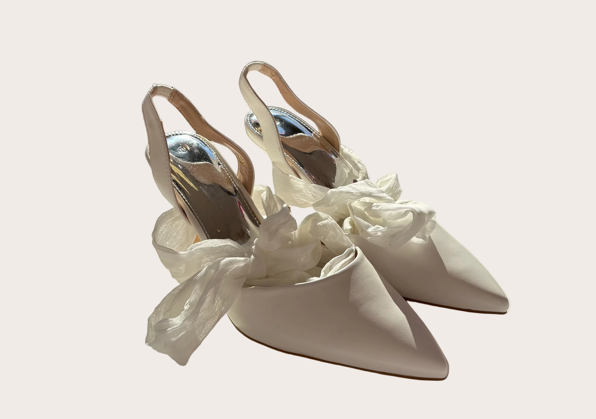 Pair of white high-heeled shoes with decorative ribbons on a light surface.